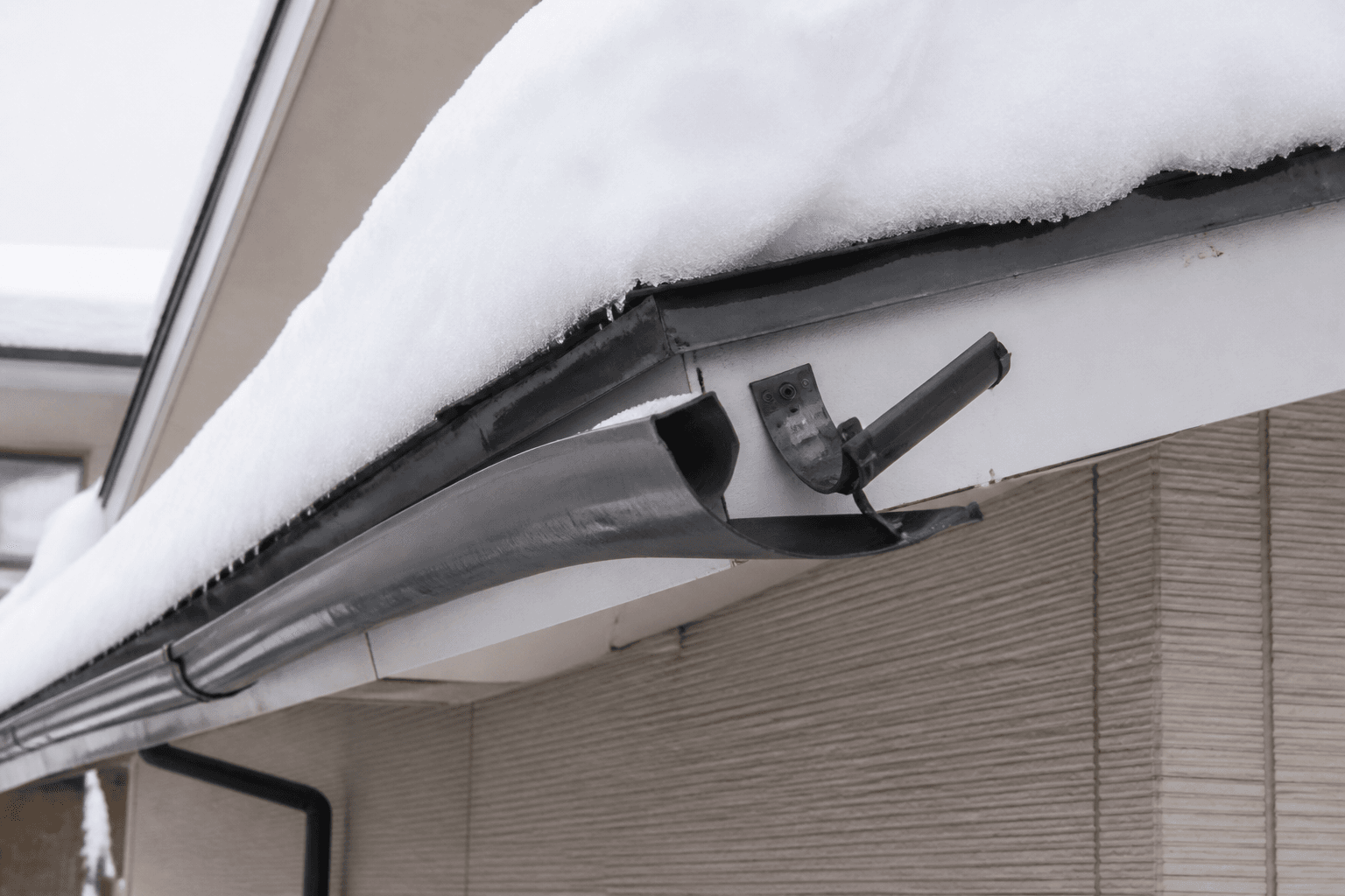 大雪の重みで歪んでしまった雨樋の写真。金具から外れかかっている様子が分かるもの。]