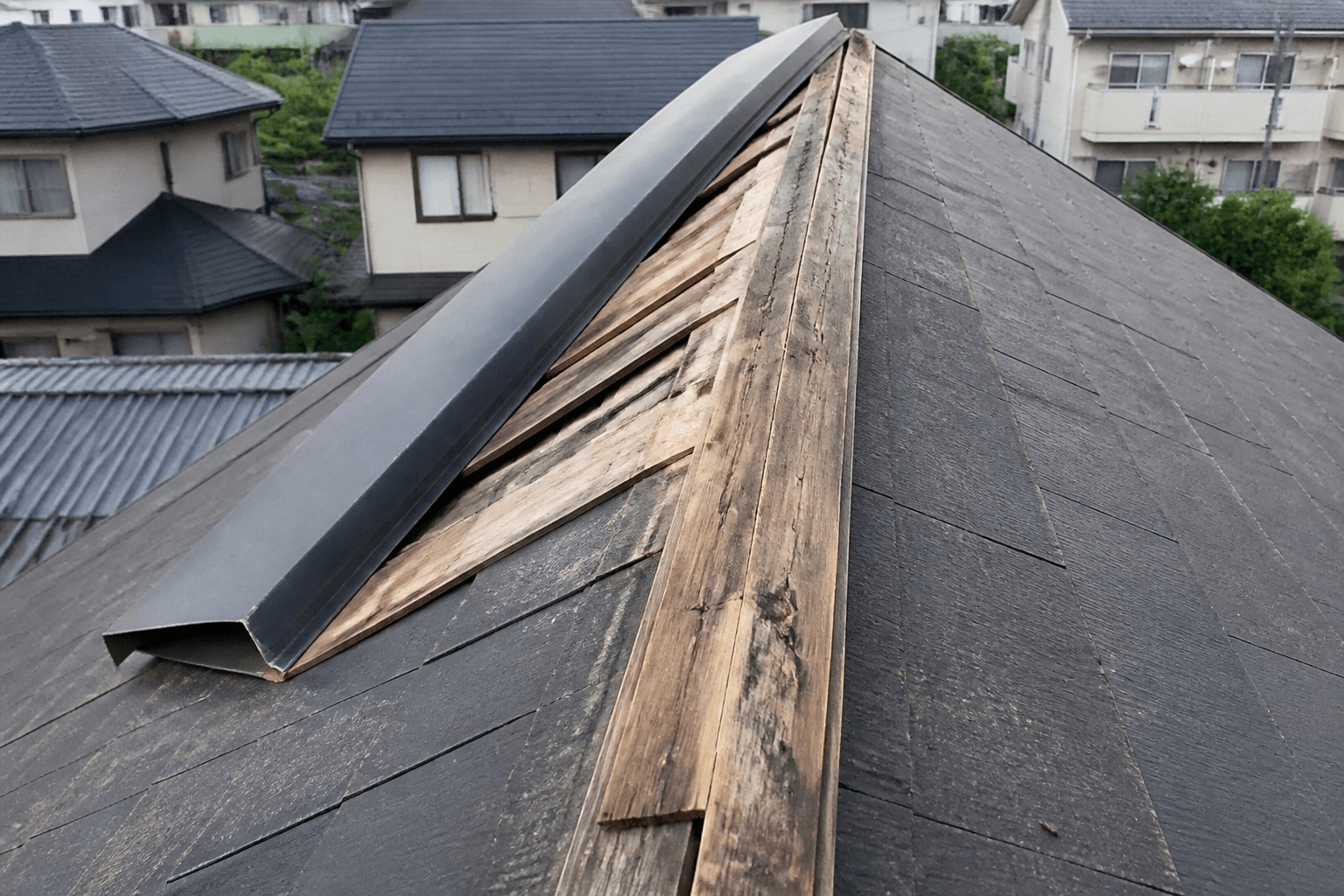 台風の強風によって剥がれてしまった棟板金の写真。屋根の頂上部分がめくれている様子が分かるもの。]
